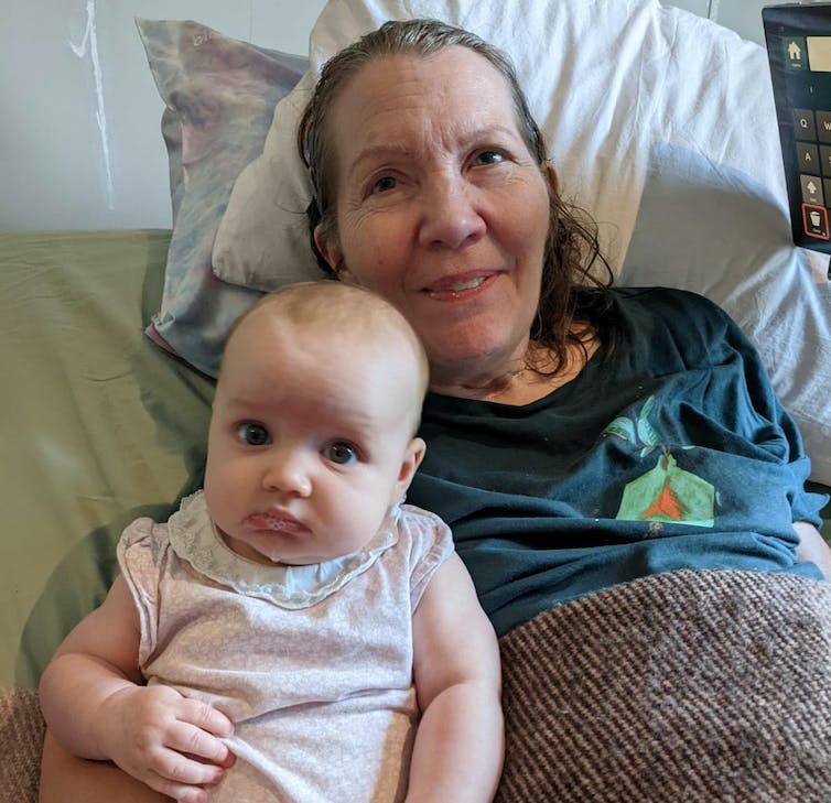 Woman sits with baby next to her on a bed.