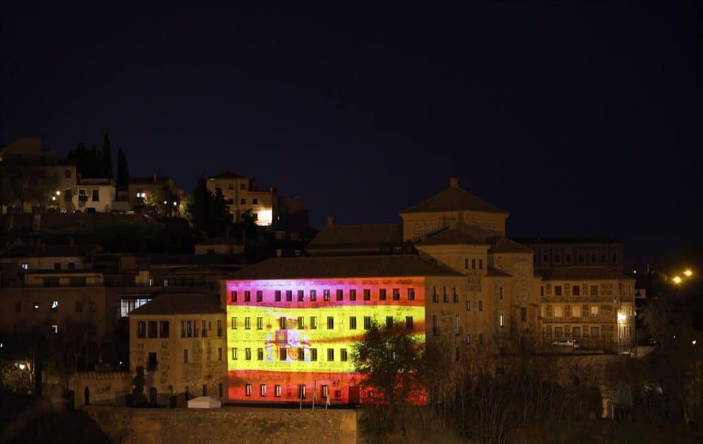 Una imagen en movimiento de la bandera de España ilumina la fachada de las Cortes de C-LM por el Día de la Constitución