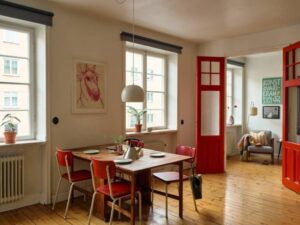 Comedor con sillas rojas vintage y puertas dobles lacadas en rojo en piso escandinavo - rojo vintage