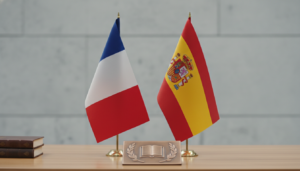 Bandera de Francia y bandera de España juntas sobre mesa de madera, fondo neutro, sin personas, contexto institucional y e...
