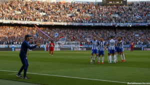 Football match in a stadium, a coach in a tracksuit giving instructions on the sideline while players celebrate a goal on ...