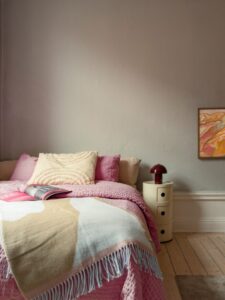 Dormitorio nórdico con cama colorida en rosa y colcha de gofre, estanterías de madera y lámina de Picasso en Estocolmo