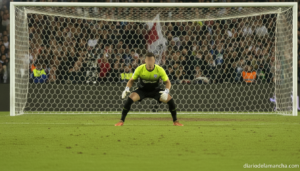 Soccer goalkeeper in team uniform positioned in front of goal net, stadium lights, football pitch with green grass, match ...