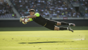 A goalkeeper in football kit making a save dive on a green football pitch. Soccer goalkeeper catching the ball, dynamic ac...