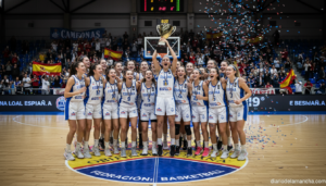 Female young basketball players celebrating a championship victory on an indoor court in Spain, team huddle with trophy, p...