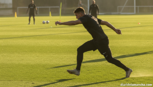 Football defender in training session on a green grass pitch, side view, athletic posture, no visible faces, sports photog...