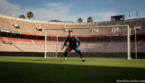 A football goalkeeper in training on a grass pitch, wearing gloves and goalkeeper jersey, making a save or standing ready ...