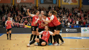Women's futsal team celebrating a goal in an indoor sports hall, players in team jerseys, emotional celebration, crowd wat...