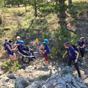 Grupo de mujeres caminando por un sendero de montaña en la Serranía de Cuenca acompañando una silla Joëlette