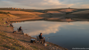 Editorial photo of a calm reservoir in rural Castilla-La Mancha, Spain, at golden hour with anglers fishing from the shore...
