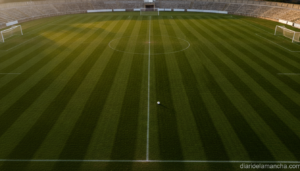 Wide shot of an empty regional football stadium pitch at golden hour in Castilla-La Mancha, Spain, green grass freshly mow...