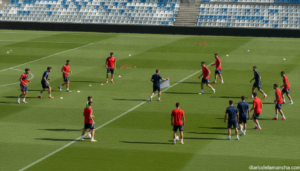Photojournalistic wide shot of a national football team training session on a bright green pitch, players in red and dark ...