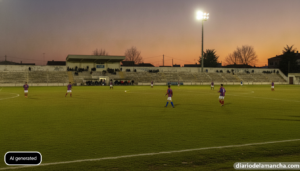 Wide realistic photojournalistic shot of a small-town Spanish amateur football stadium at dusk during a preseason friendly...
